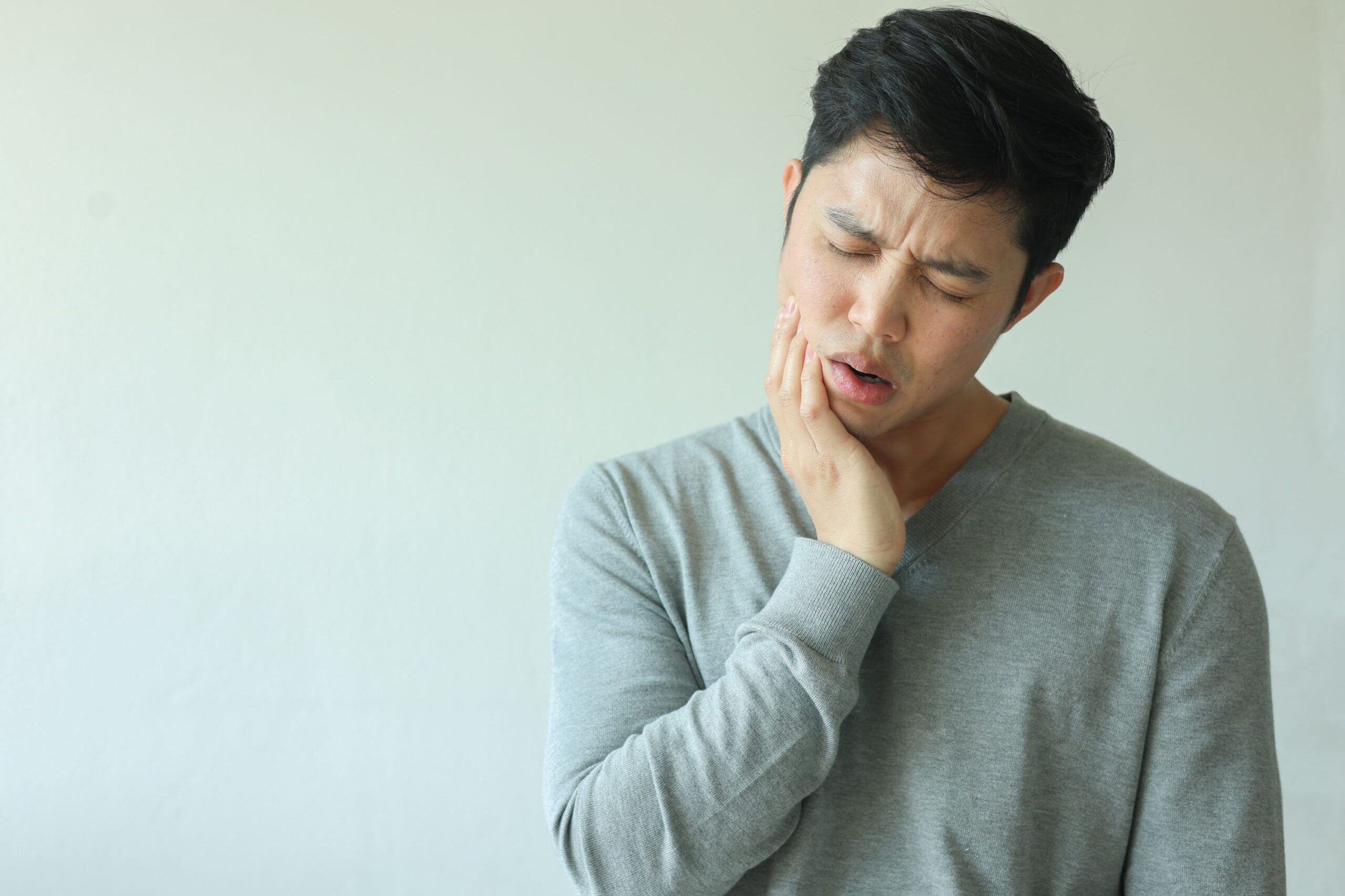 Man in gray shirt touching hand to jaw in pain